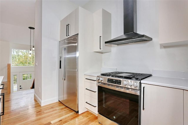 kitchen featuring white cabinets, hanging light fixtures, wall chimney exhaust hood, appliances with stainless steel finishes, and light hardwood / wood-style floors