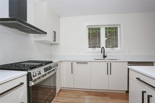 kitchen featuring sink, stainless steel range, wall chimney exhaust hood, light hardwood / wood-style flooring, and white cabinets