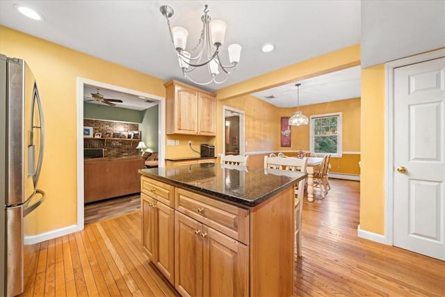 kitchen featuring ceiling fan with notable chandelier, decorative light fixtures, a center island, light hardwood / wood-style floors, and stainless steel refrigerator