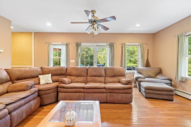 living room featuring ceiling fan, plenty of natural light, light hardwood / wood-style floors, and a baseboard heating unit