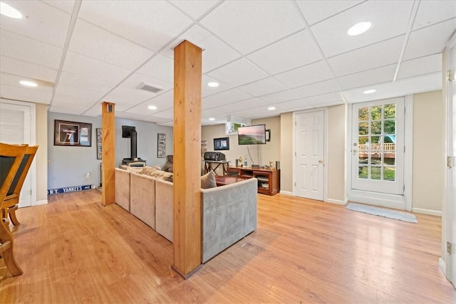 living room with a wood stove, a drop ceiling, and light wood-type flooring