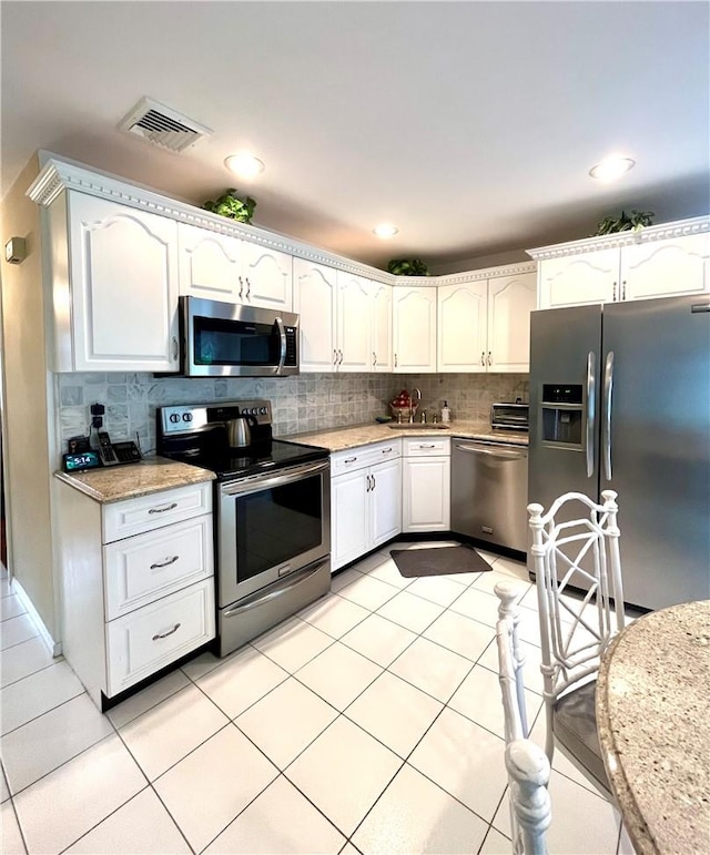 kitchen with light tile patterned flooring, white cabinetry, stainless steel appliances, and tasteful backsplash