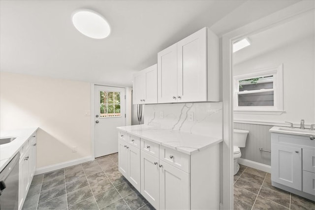 kitchen featuring white cabinetry, sink, light stone counters, stainless steel dishwasher, and decorative backsplash