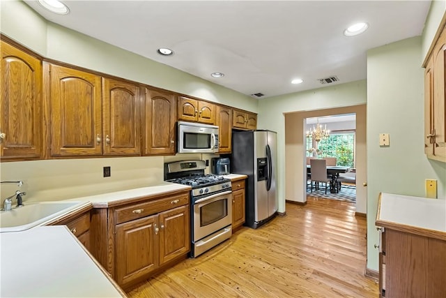 kitchen featuring sink, an inviting chandelier, stainless steel appliances, and light hardwood / wood-style floors