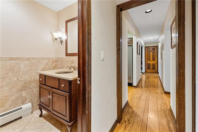 interior space featuring sink, tile walls, baseboard heating, and light hardwood / wood-style flooring