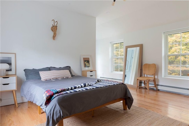 bedroom featuring light hardwood / wood-style floors, baseboard heating, and multiple windows