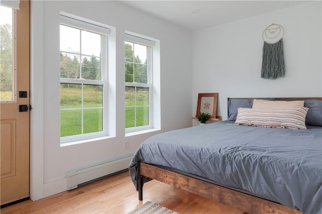 bedroom featuring light hardwood / wood-style floors, baseboard heating, and multiple windows