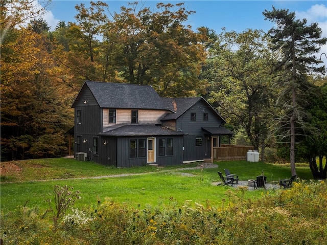 rear view of property featuring a lawn, central AC, and a fire pit