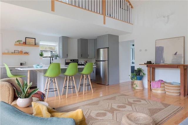 kitchen with a high ceiling, stainless steel appliances, gray cabinets, and light hardwood / wood-style floors