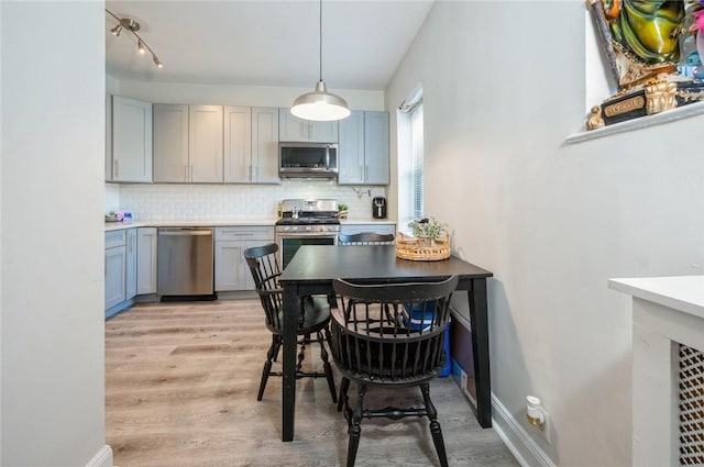 kitchen with backsplash, stainless steel appliances, hanging light fixtures, and light hardwood / wood-style floors