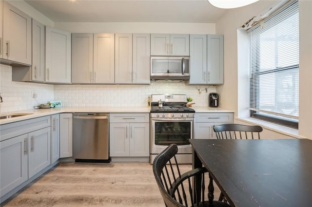 kitchen with gray cabinetry, light wood-type flooring, appliances with stainless steel finishes, and tasteful backsplash