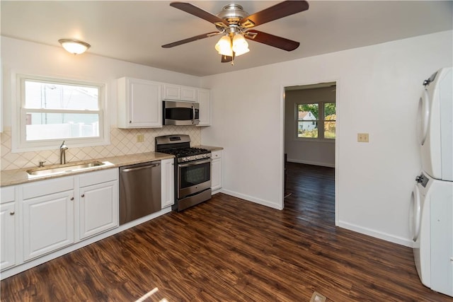 kitchen featuring white cabinetry, sink, stacked washing maching and dryer, dark hardwood / wood-style floors, and appliances with stainless steel finishes