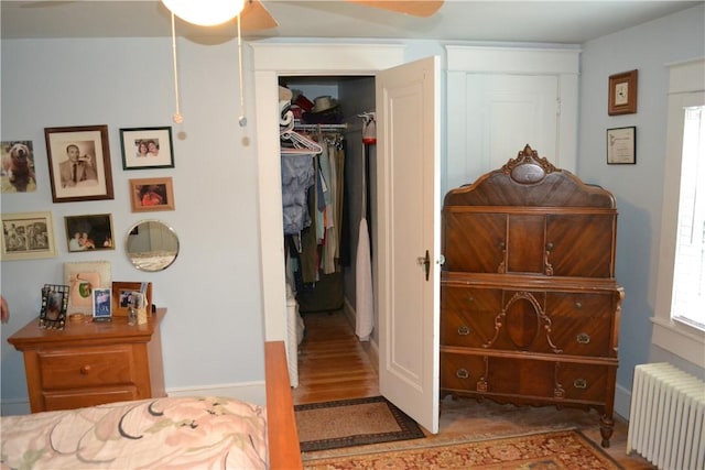 bedroom with hardwood / wood-style floors, ceiling fan, radiator heating unit, and a closet