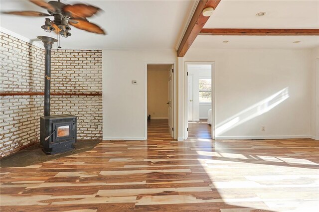 unfurnished living room with a wood stove, ceiling fan, beamed ceiling, light hardwood / wood-style floors, and brick wall