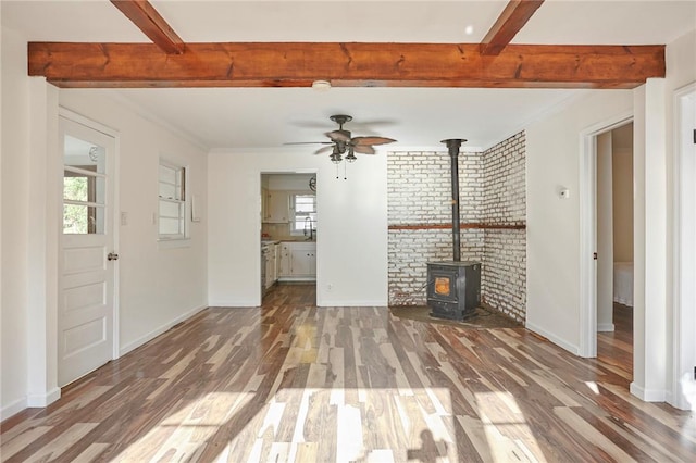 unfurnished living room featuring ornamental molding, ceiling fan, dark wood-type flooring, beamed ceiling, and a wood stove