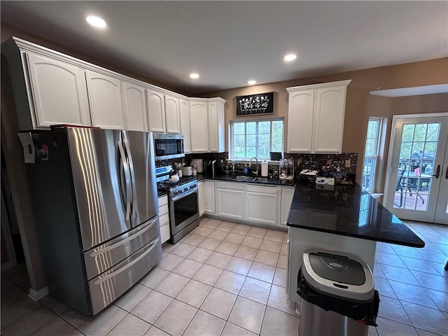 kitchen with appliances with stainless steel finishes, tasteful backsplash, sink, light tile patterned floors, and white cabinetry