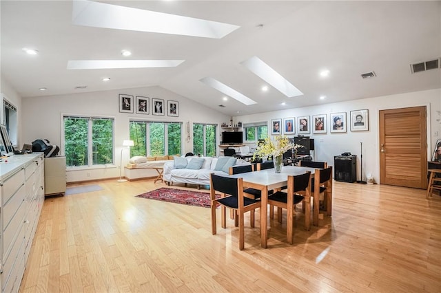 dining room featuring vaulted ceiling with skylight, a wealth of natural light, and light hardwood / wood-style flooring