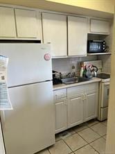 kitchen with white refrigerator, light tile patterned floors, sink, and stainless steel range