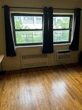 empty room with light wood-type flooring, a wall unit AC, and radiator