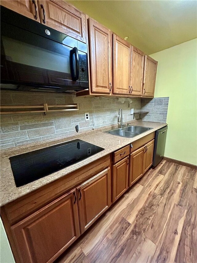 kitchen with black appliances, light wood-type flooring, sink, and tasteful backsplash