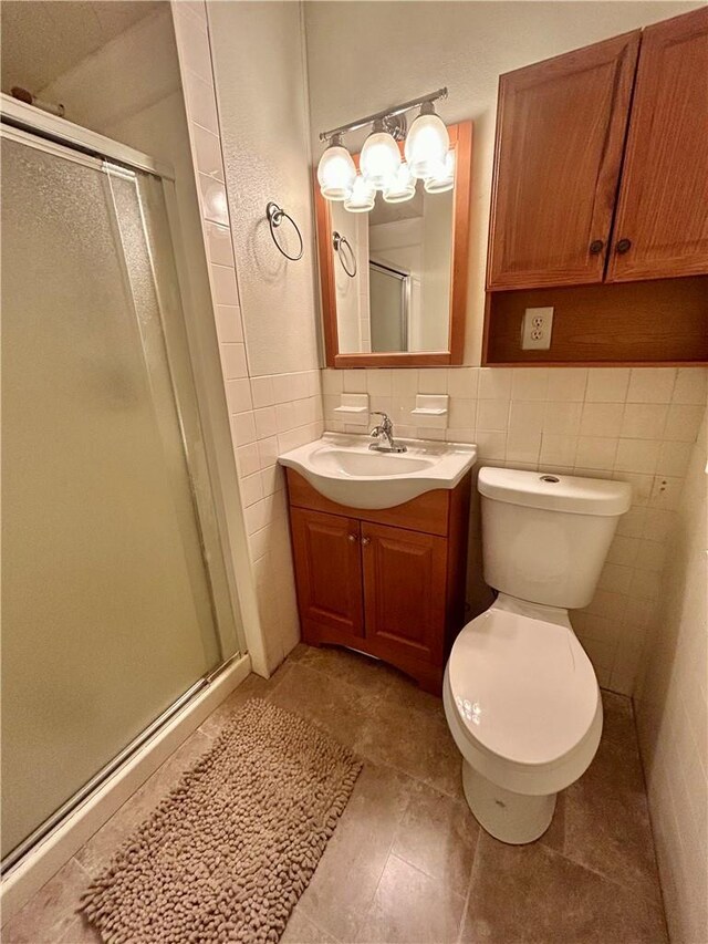 bathroom with tile patterned flooring, toilet, vanity, a shower with shower door, and tile walls