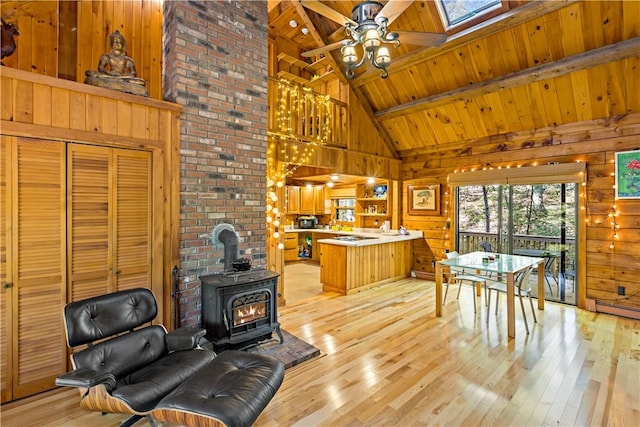 living room featuring light wood-type flooring, a skylight, a wood stove, and high vaulted ceiling