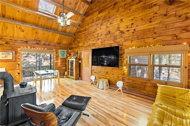 living room with wooden walls, a skylight, a wood stove, and light hardwood / wood-style floors