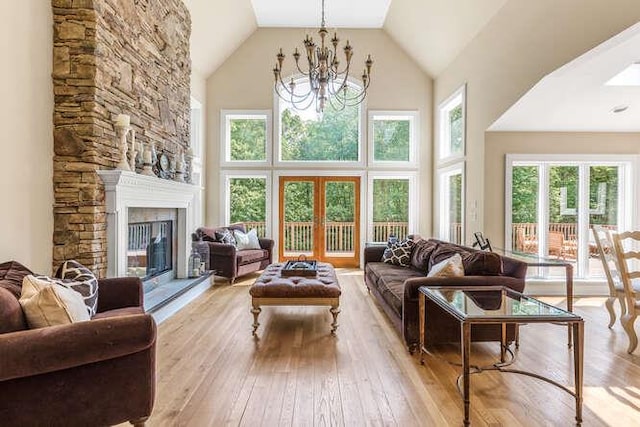 living room featuring light hardwood / wood-style flooring, high vaulted ceiling, a notable chandelier, and a stone fireplace