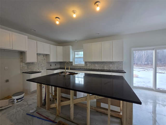 kitchen with marble finish floor, white cabinetry, backsplash, and a sink