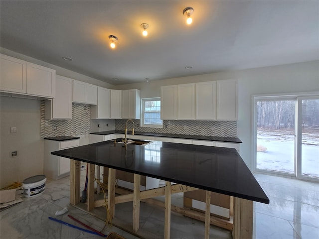 kitchen featuring tasteful backsplash, dark countertops, a sink, and white cabinets