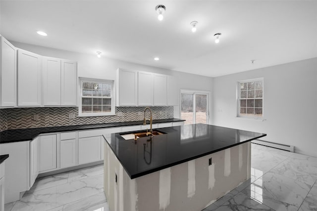 kitchen featuring a sink, decorative backsplash, marble finish floor, dark countertops, and a baseboard heating unit