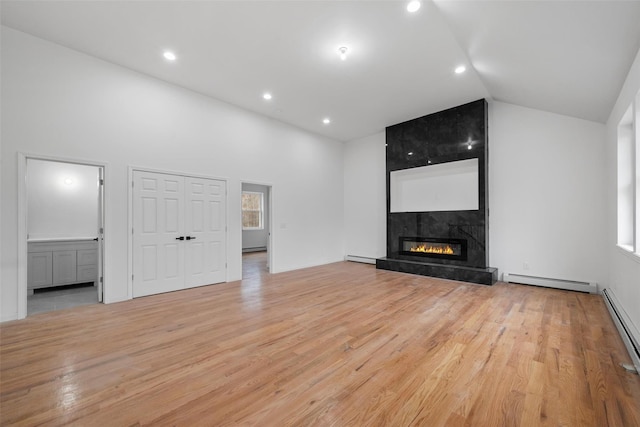 unfurnished living room with a high end fireplace, vaulted ceiling, light wood finished floors, and baseboard heating