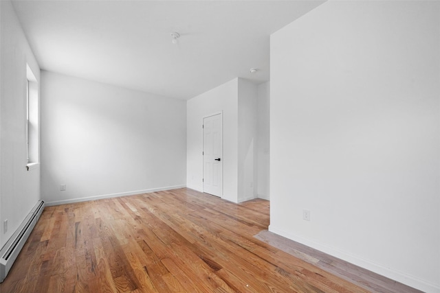 spare room with baseboards, wood finished floors, and a baseboard heating unit