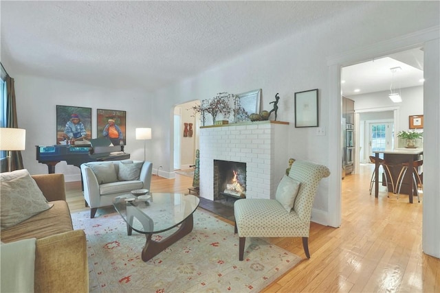 living room with light wood-style flooring, a fireplace, arched walkways, and a textured ceiling