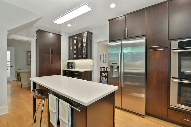 kitchen with glass insert cabinets, appliances with stainless steel finishes, a center island, light countertops, and light wood-type flooring