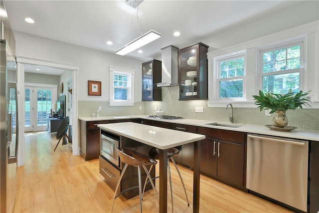 kitchen featuring dark brown cabinetry, stainless steel appliances, a sink, light countertops, and glass insert cabinets