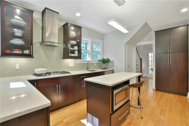 kitchen with light countertops, hanging light fixtures, glass insert cabinets, appliances with stainless steel finishes, and ventilation hood