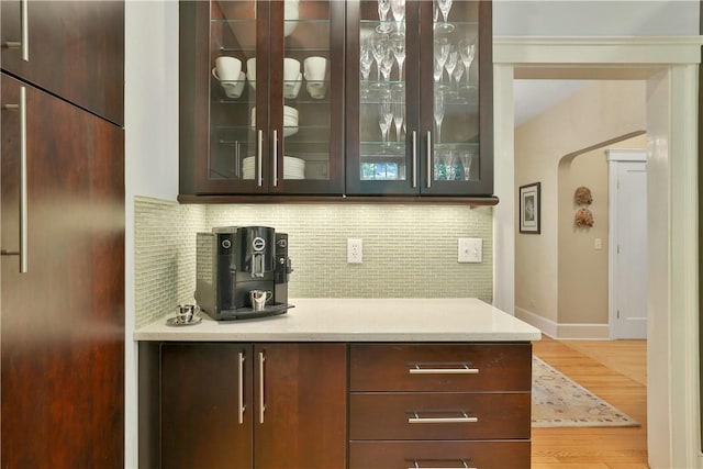 bar with arched walkways, built in fridge, baseboards, decorative backsplash, and light wood finished floors