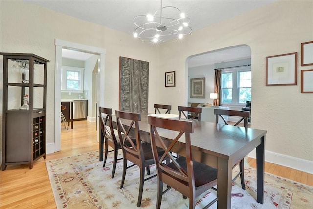 dining room with arched walkways, baseboards, a notable chandelier, and light wood finished floors