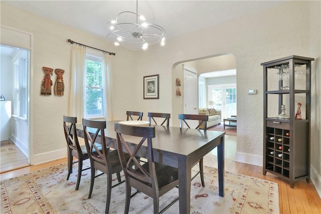 dining space with arched walkways, light wood-style flooring, a chandelier, and a wealth of natural light