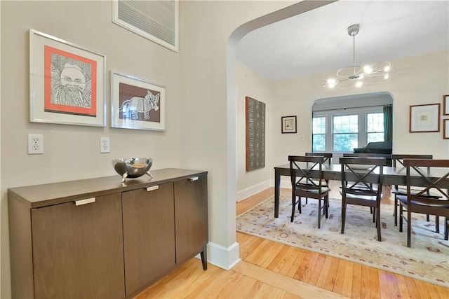 dining area featuring a chandelier, arched walkways, light wood-style flooring, and baseboards