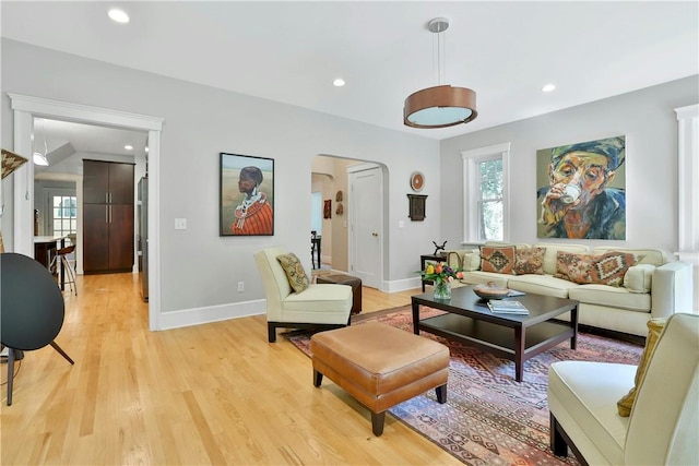 living room with a wealth of natural light, arched walkways, light wood-style flooring, and recessed lighting