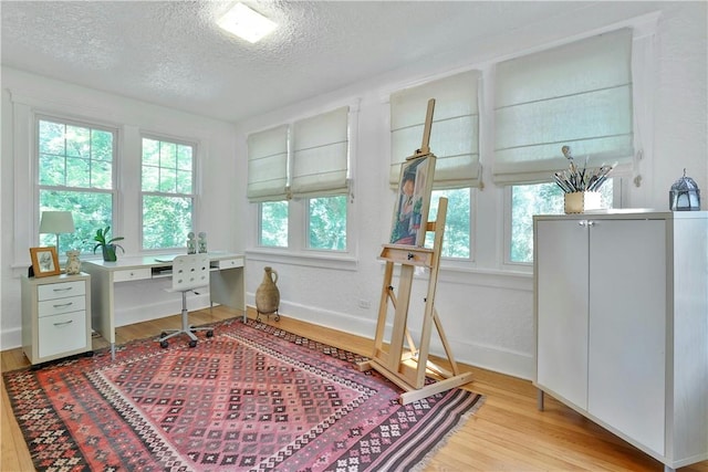 office space featuring light wood-style floors, baseboards, and a textured ceiling