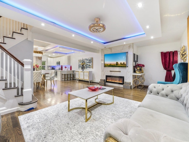 living room featuring a tray ceiling, a large fireplace, and dark wood-type flooring