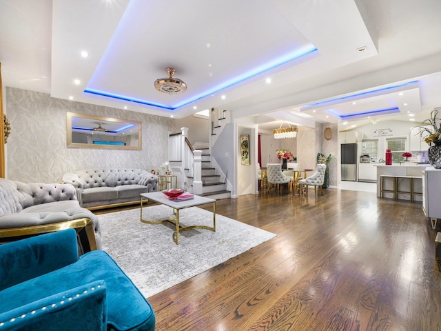 living room with a tray ceiling, dark hardwood / wood-style flooring, and ceiling fan with notable chandelier