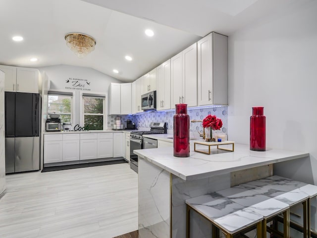 kitchen featuring a breakfast bar, white cabinets, vaulted ceiling, appliances with stainless steel finishes, and kitchen peninsula