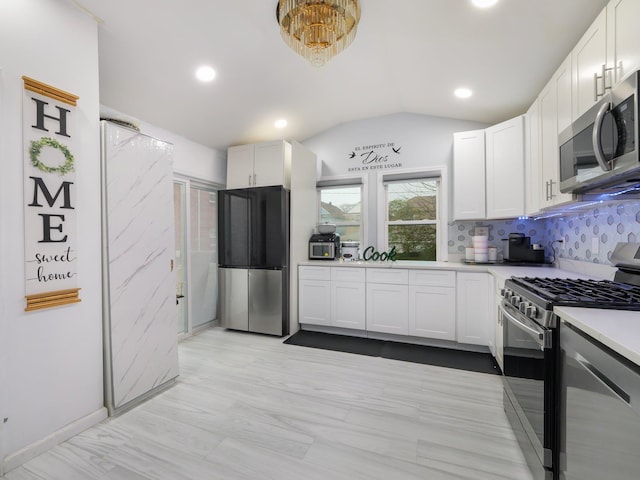 kitchen featuring white cabinets, decorative backsplash, stainless steel appliances, and vaulted ceiling