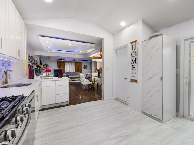 kitchen with white cabinets, sink, vaulted ceiling, light hardwood / wood-style flooring, and kitchen peninsula