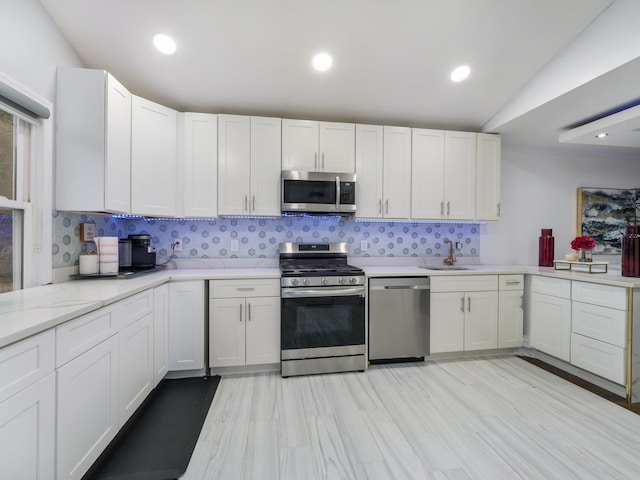 kitchen with lofted ceiling, backsplash, sink, white cabinetry, and stainless steel appliances