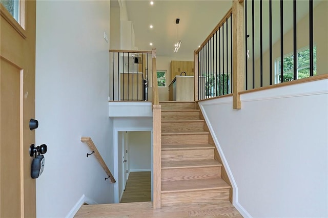 staircase with a chandelier, hardwood / wood-style floors, and a high ceiling